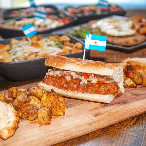 Argentinian choripán with onions and peppers, served with roasted potatoes and an empanada.