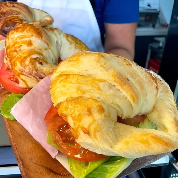 Close-up of two golden croissants filled with ham, lettuce, and tomato on a wooden board.