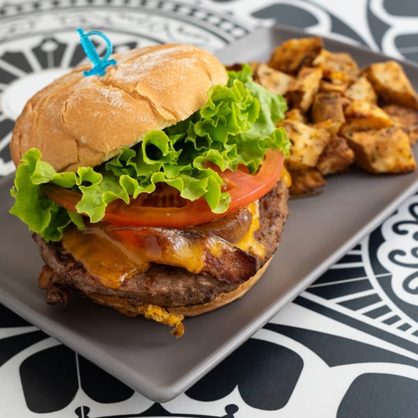 A La Bottega Miami burger with cheese, bacon, lettuce, and tomato, served with roasted potatoes.