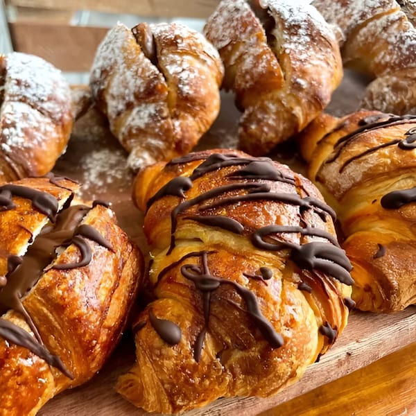 Assortment of La Bottega Miami's croissants, some dusted with powdered sugar, others drizzled with chocolate.