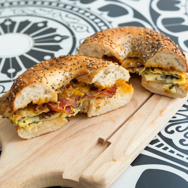 Two halves of a bagel sandwich with egg, cheese, and bacon on a wooden board.