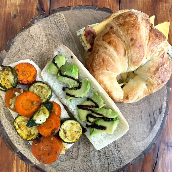 A croissant sandwich with cheese and bacon, and two baguette slices with avocado and grilled vegetables.