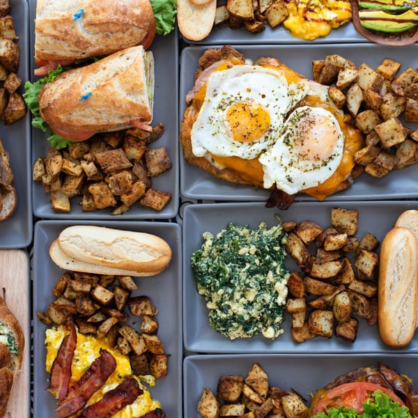 Overhead view of various Argentinian dishes including sandwiches, milanesa, scrambled eggs with bacon, and potatoes.