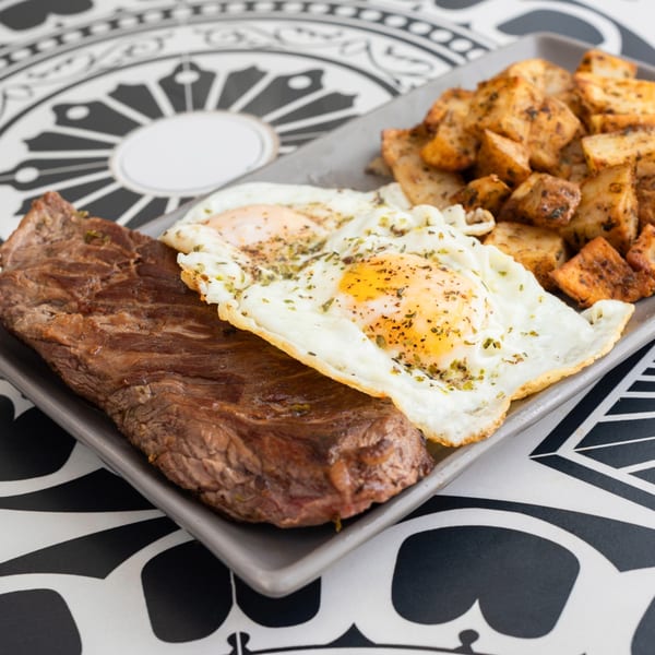 Argentinian skirt steak with two fried eggs and roasted potatoes on a gray plate.